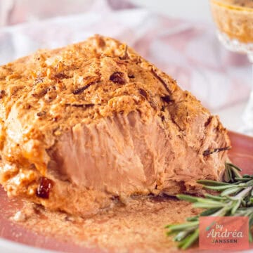 Slowcooker rollade aangesneden op een roze plank met saus ernaast