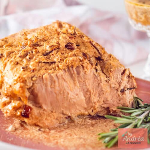 Slowcooker rollade aangesneden op een roze plank met saus ernaast