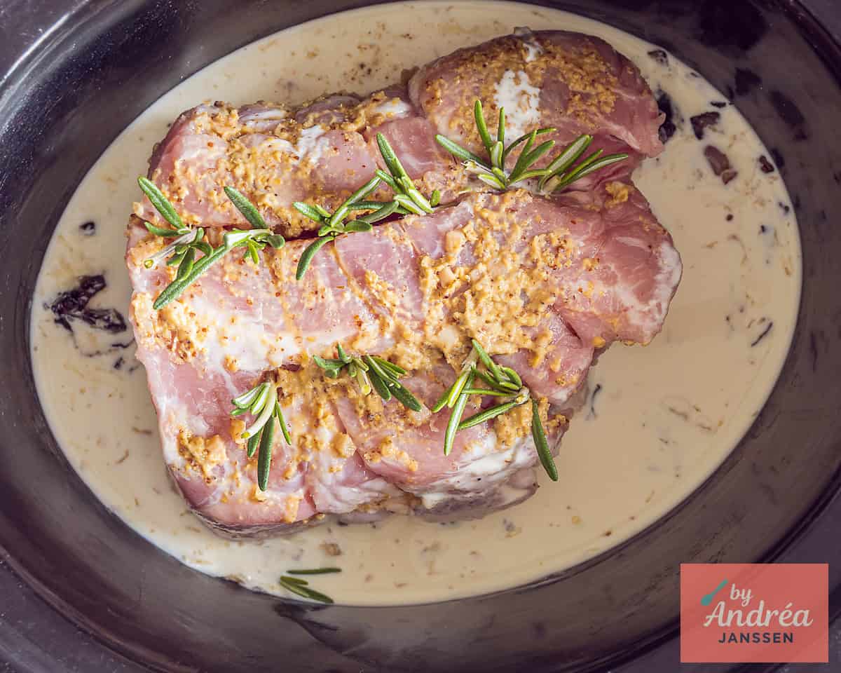 Een slowcooker met rollade gevuld met rozemarijn en mosterd knoflook marinade in room