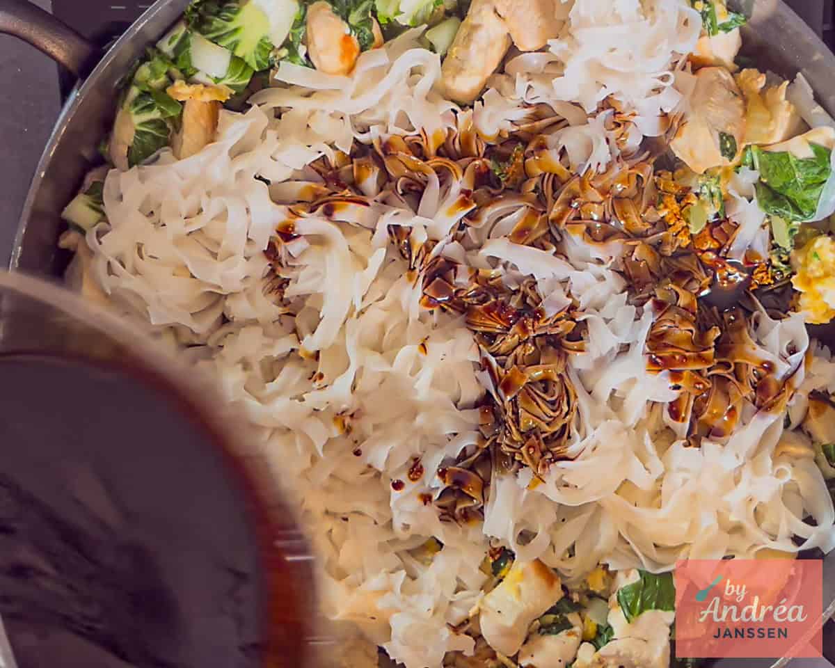 Voeg saus toe aan de pan met de rijstnoedels met kip en paksoi