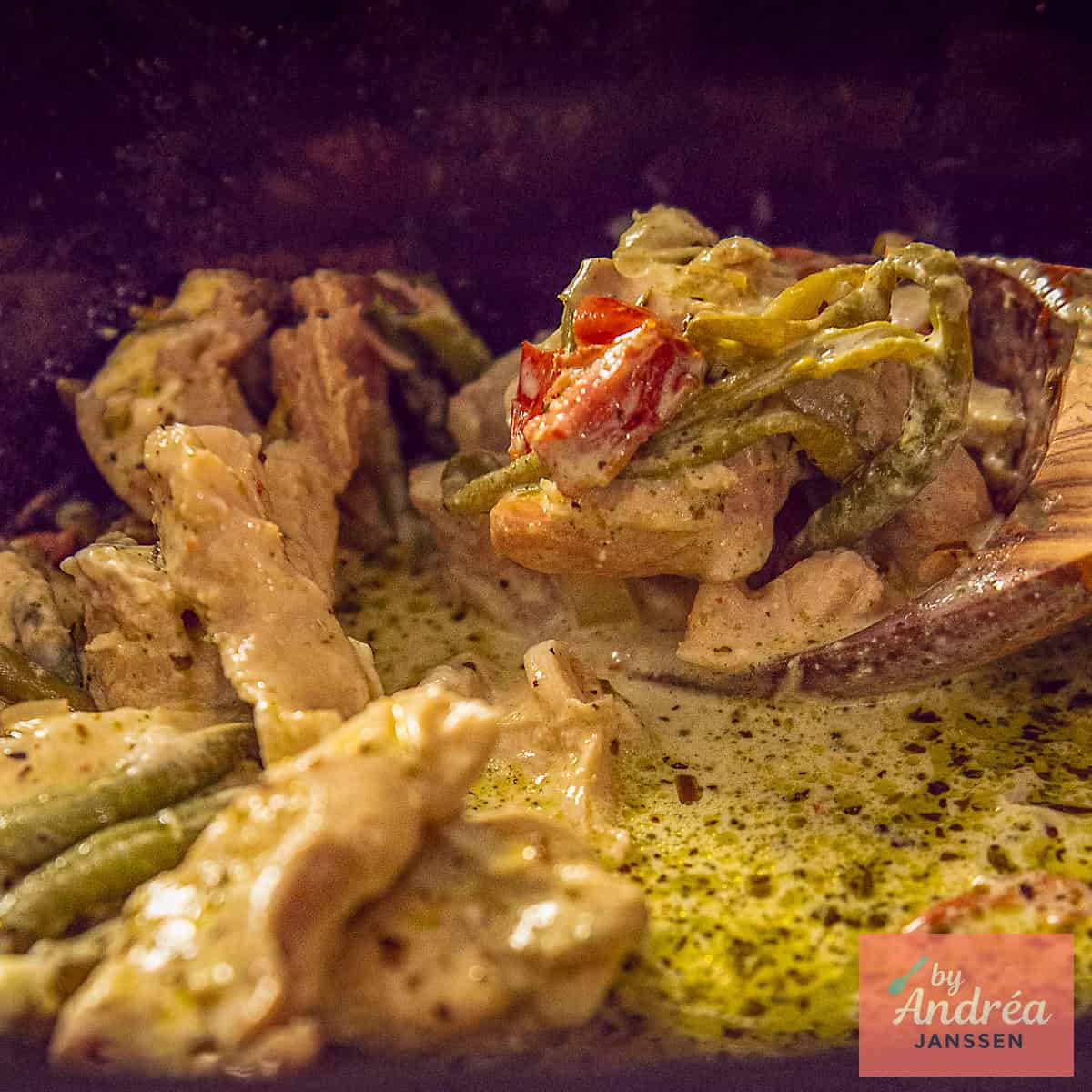 Een vierkante foto met een slowcooker met Toscaanse kip waaruit een lepel wordt geschept.