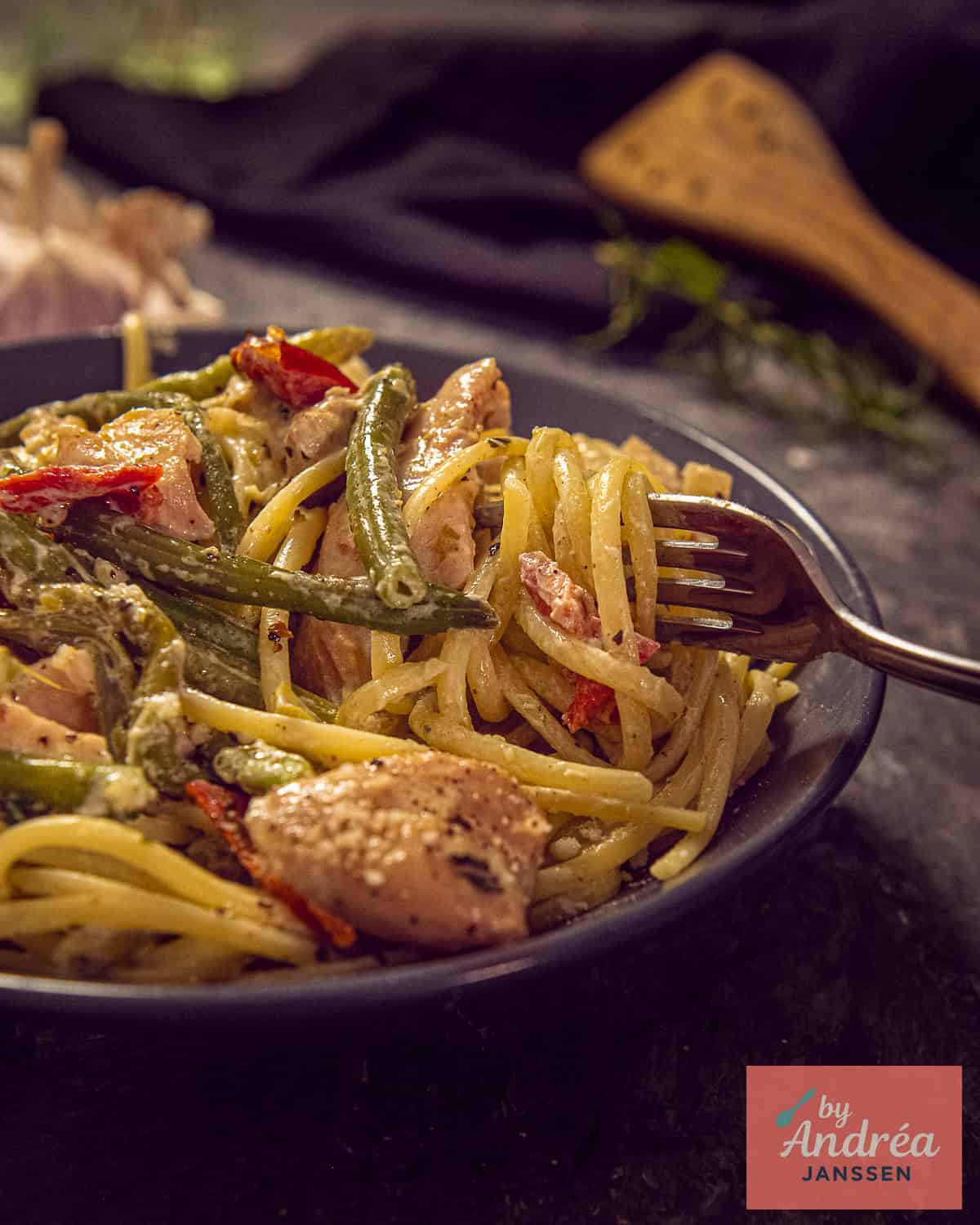 Een grijs bord met pasta en Toscaanse kip uit de slowcooker met boontjes