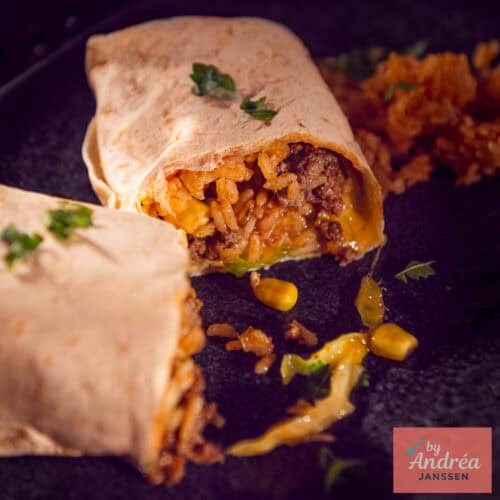 Een vierkante foto met een opengesneden burrito met een vulling van rijst, mais, gehakt, kaas, kool, tomaat en ui.
