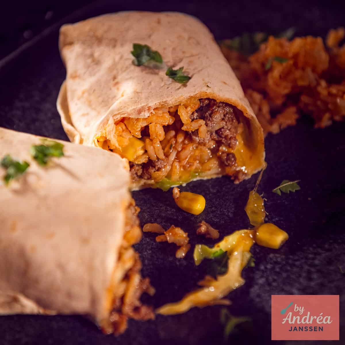 Een vierkante foto met een opengesneden burrito met een vulling van rijst, mais, gehakt, kaas, kool, tomaat en ui.