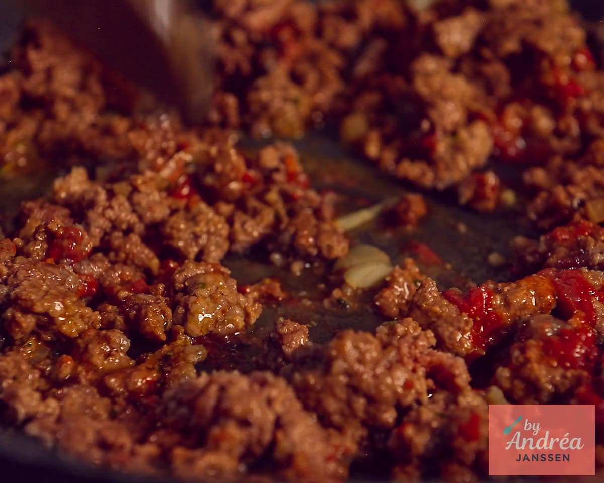 Een koekenpan met rul gebakken rundergehakt met smaakmakers zoals tomatenpuree en ui