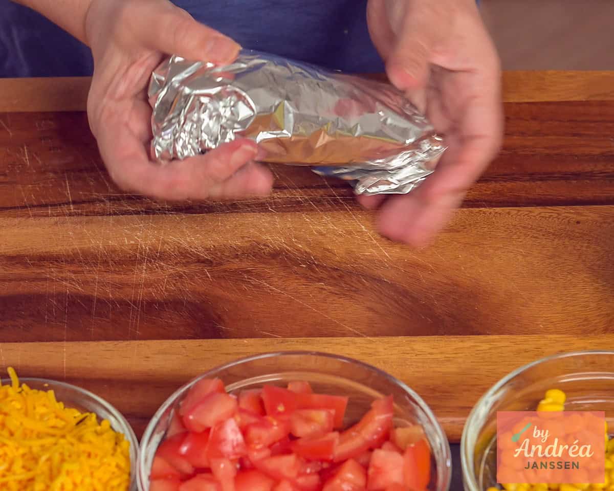 De burrito in folie gevouwen, alle ingredienten voor de vulling staan in de voorgrond