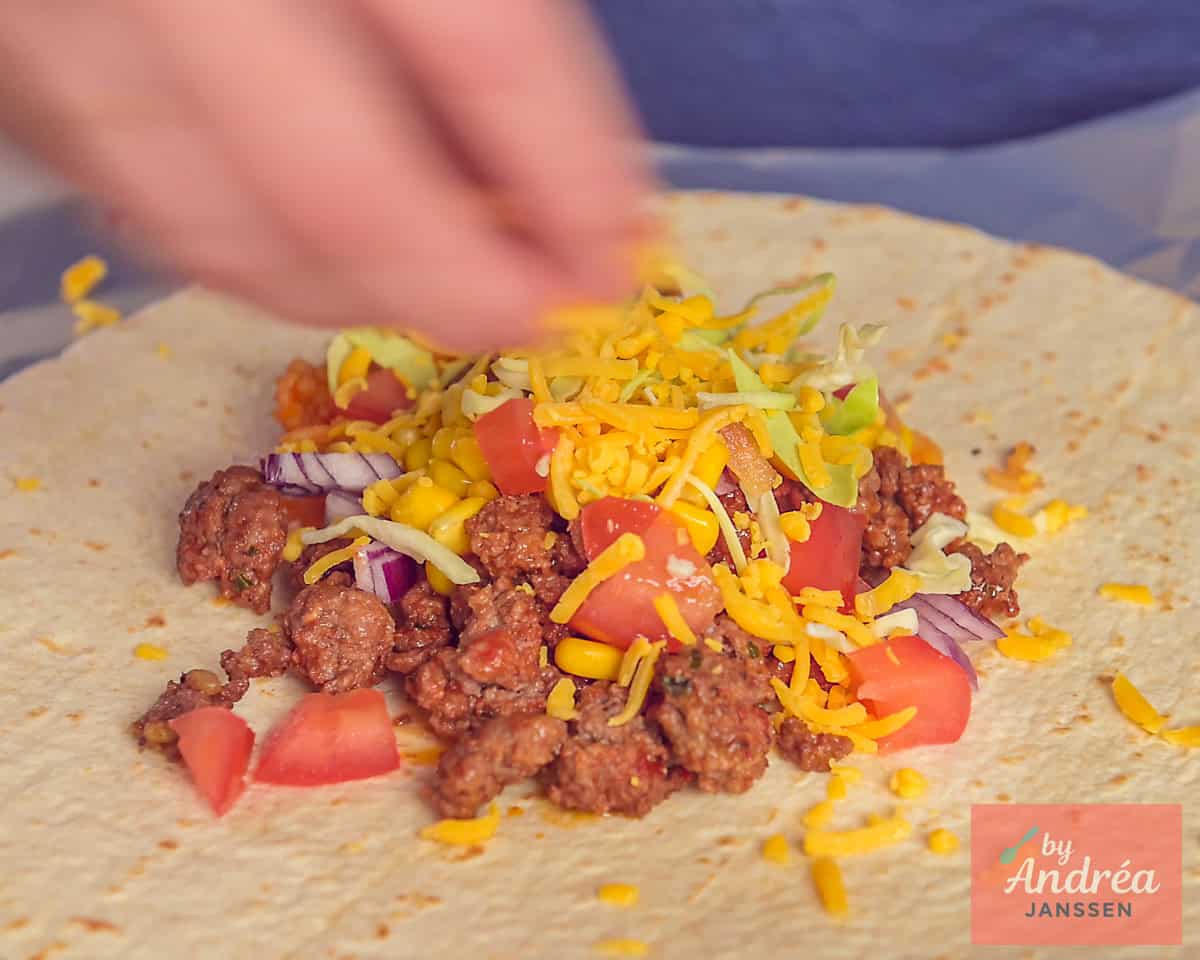 Een wrap met daarop de vulling van gehakt, tomaat, kool, mais, ui en kaas erop