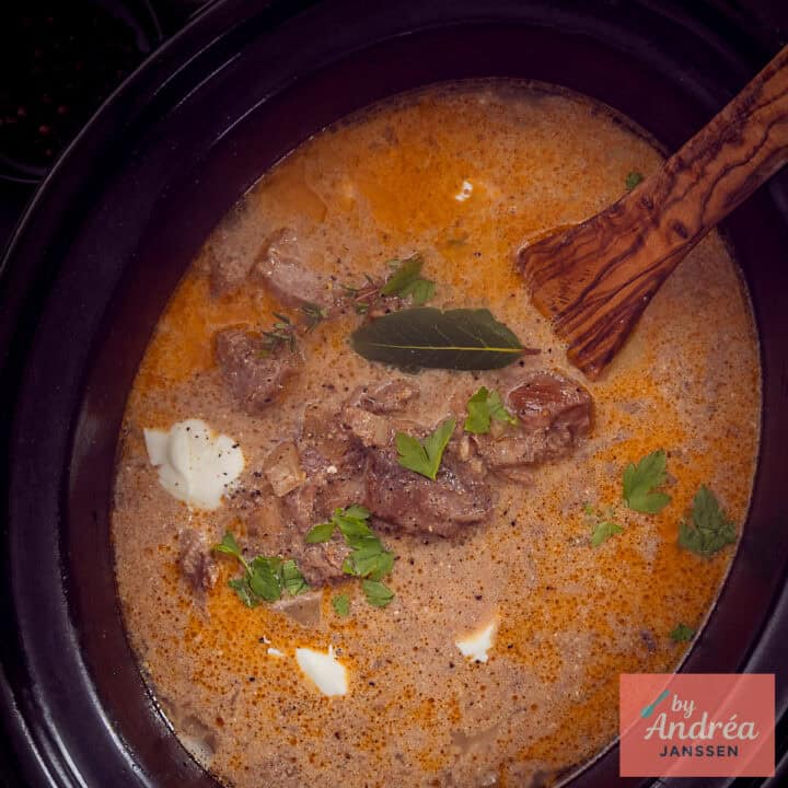 Een vierkante foto van een deel van een slowcooker gevuld met stroganoff met rundvlees.