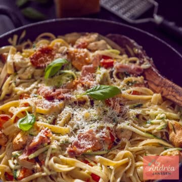 Een vierkante foto van een hapjespan met pasta, kip, romige saus met bacon