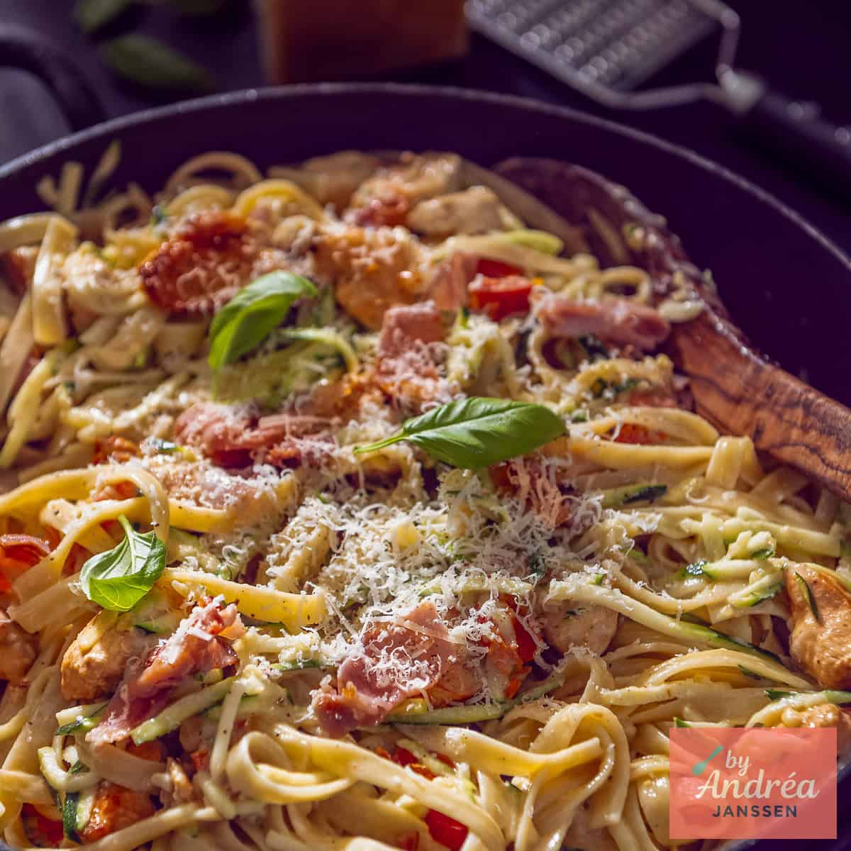 Een vierkante foto van een hapjespan met pasta, kip, romige saus met bacon