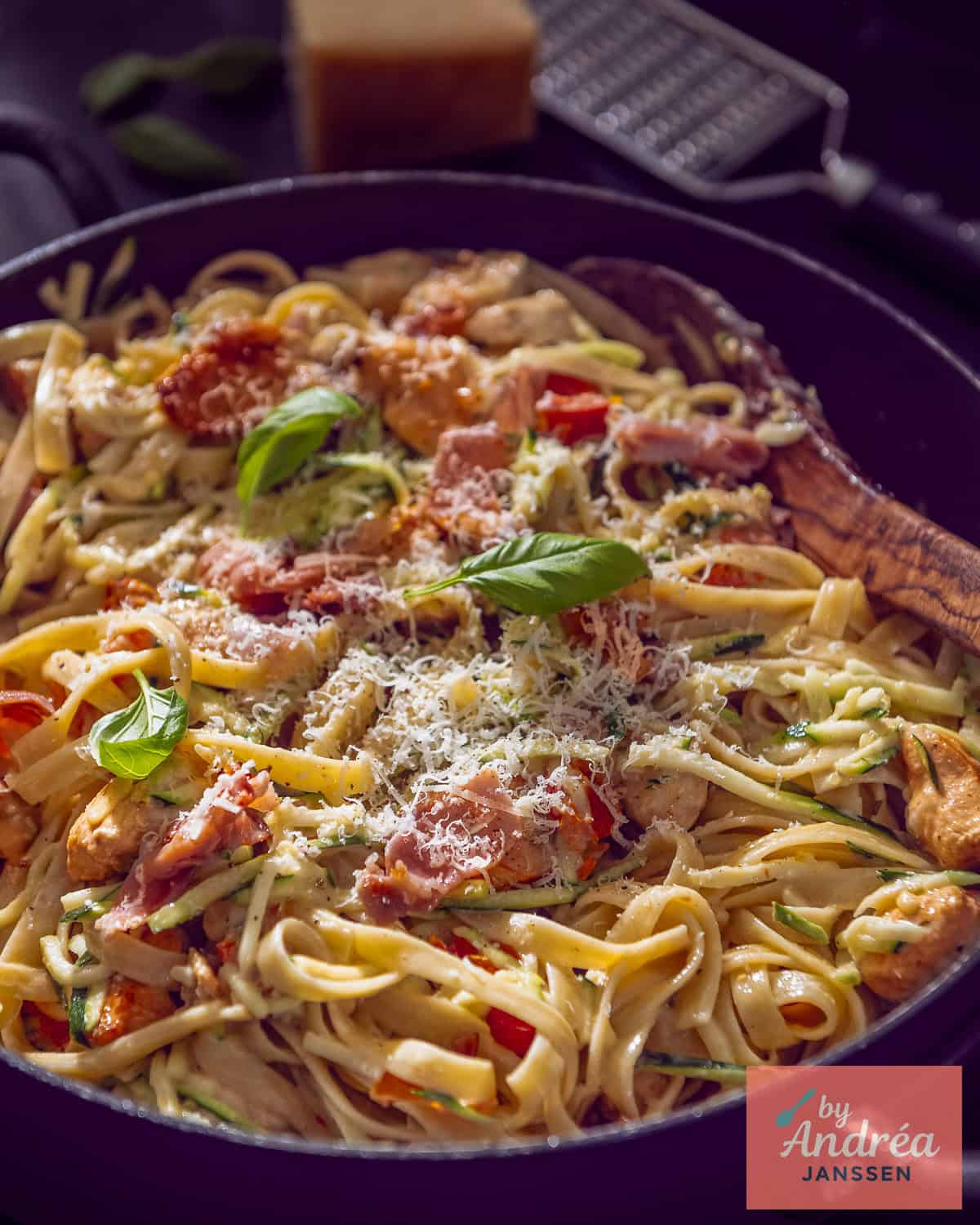 Een deel van een hapjespan gevuld met fettuccine pasta met een romige saus met bacon, zongedroogde tomaten en bacon.