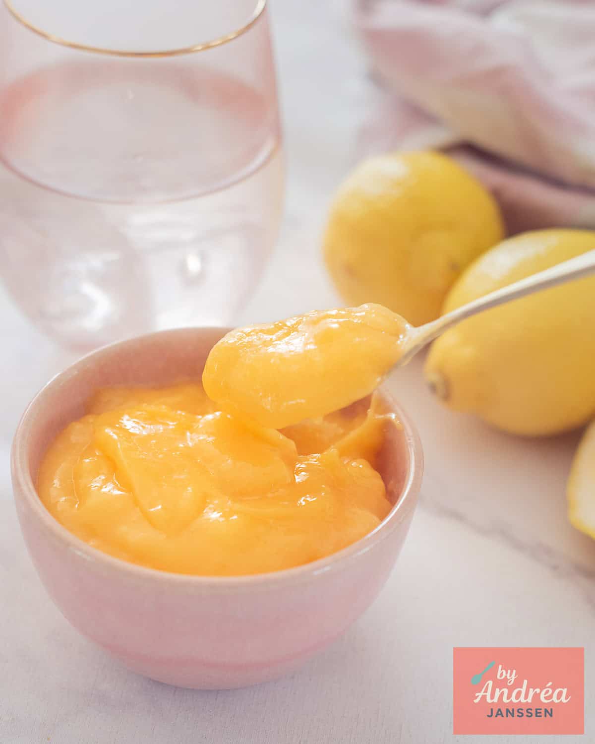 Een roze kom met lemon curd, een lepel pakt een schep eruit.