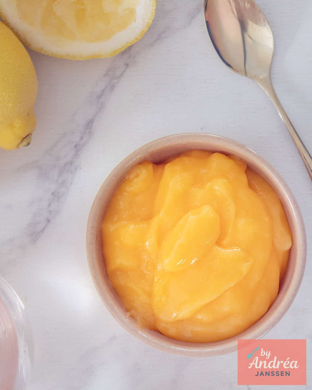 Een foto van bovenaf van een kom met lemon curd op een witte ondergrond.