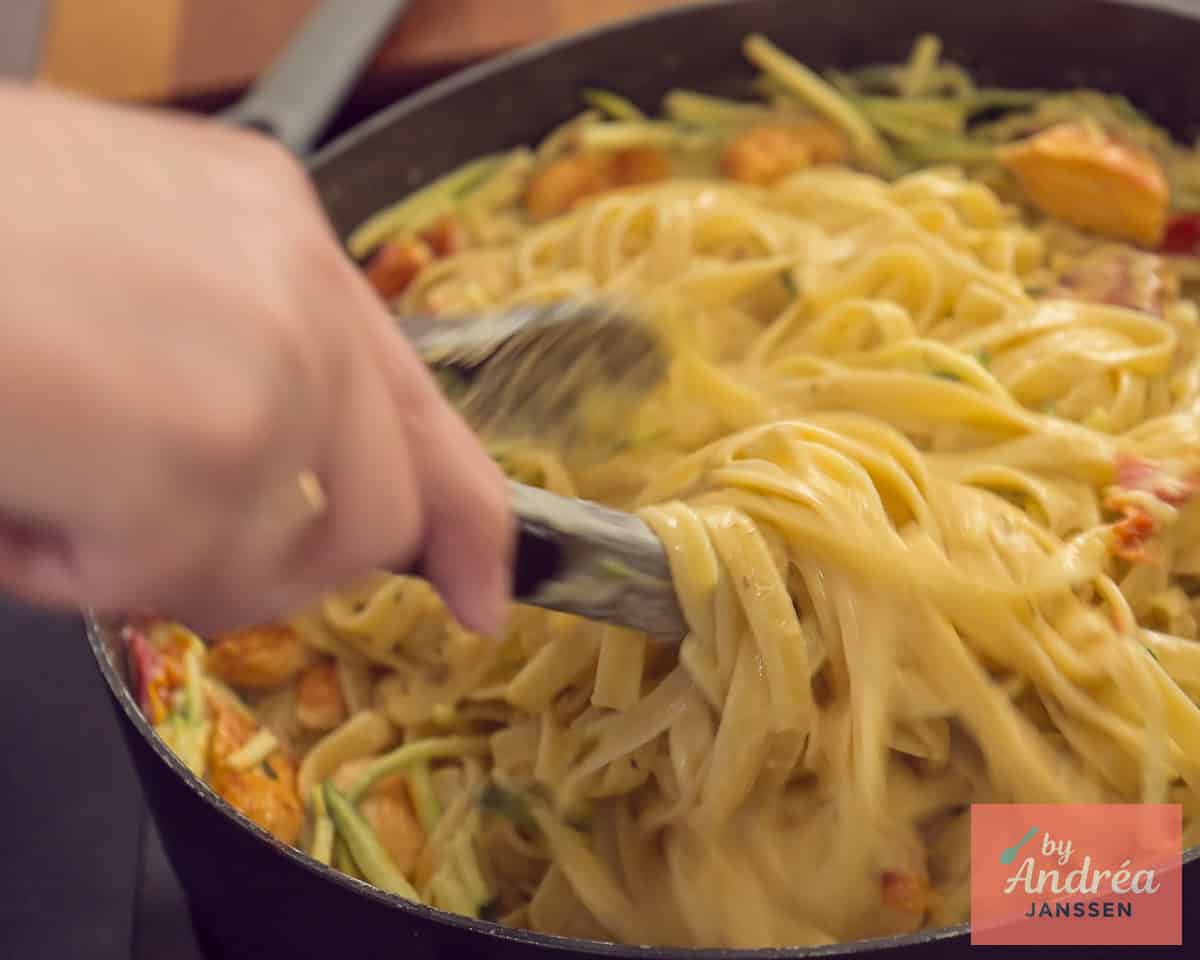 Een hapjespan met pasta met kip, romige saus en bacon die door elkaar wordt gehusseld
