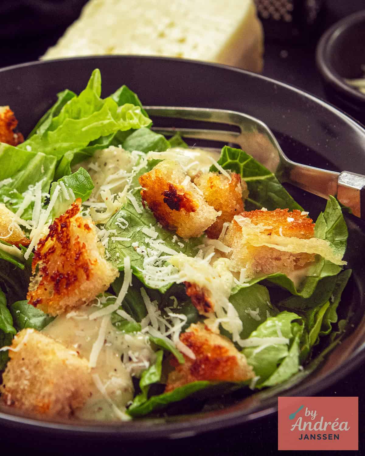Close-up van caesar salad met goudbruine zelfgemaakte croutons, verse Parmezaanse kaas en romige dressing, met een stuk Parmezaan op de achtergrond