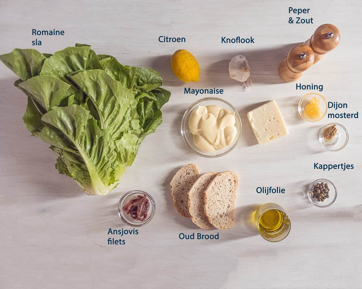 Ingredienten Caesar Salade met Zelfgemaakte Dressing op een beige ondergrond met tekstbeschrijving.