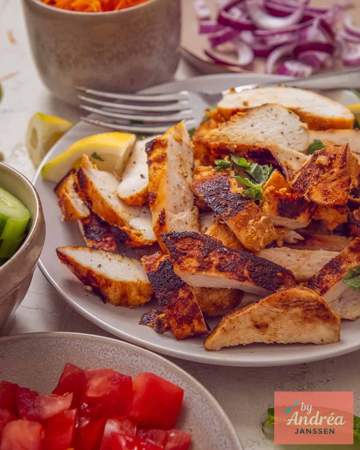 Gegrilde kipshoarma reepjes op een bord met vork, omringd door tomaat, komkommer en rode ui als toppings