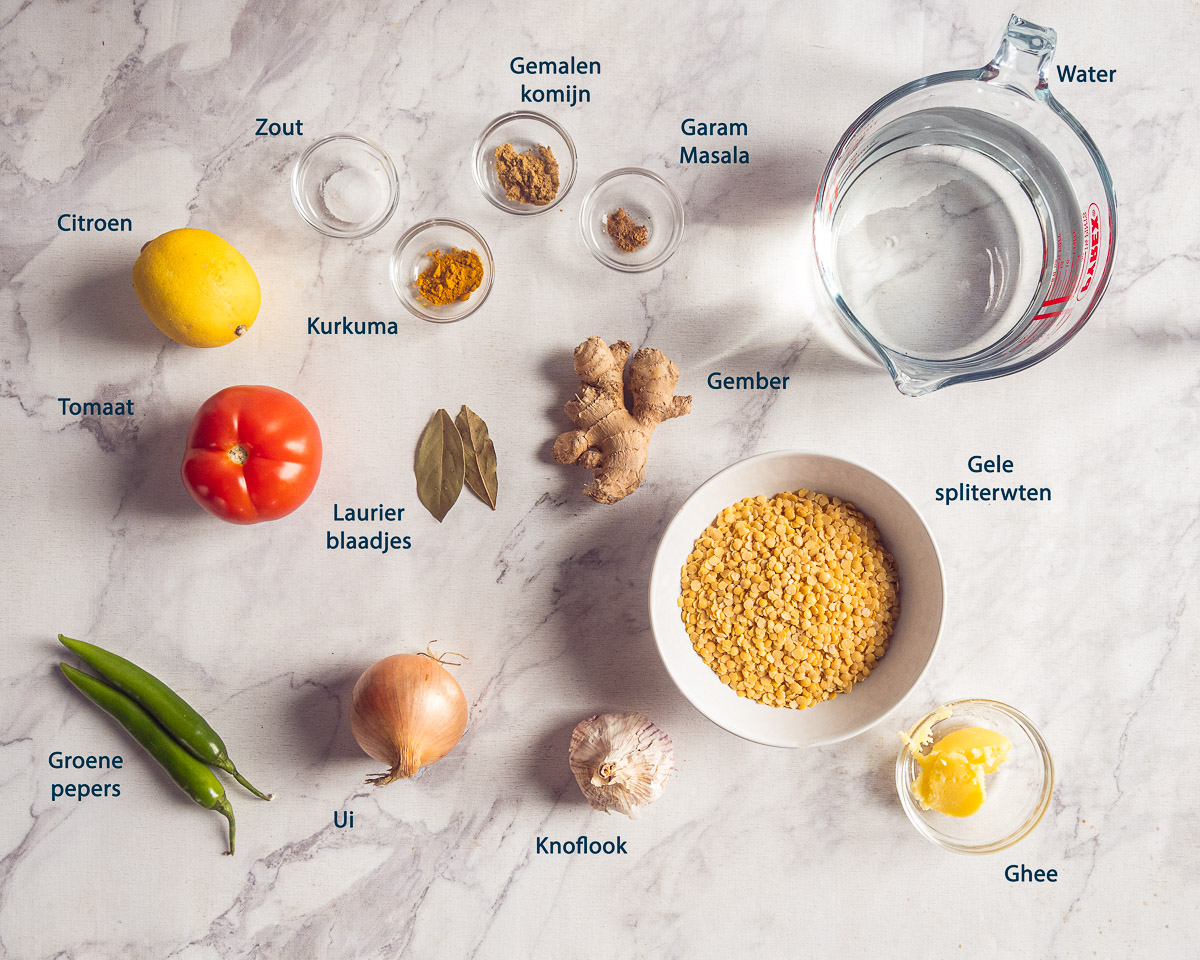 Ingrediënten voor gele spliterwtendahl, waaronder spliterwten, tomaat, gember en specerijen, met Nederlandse labels.