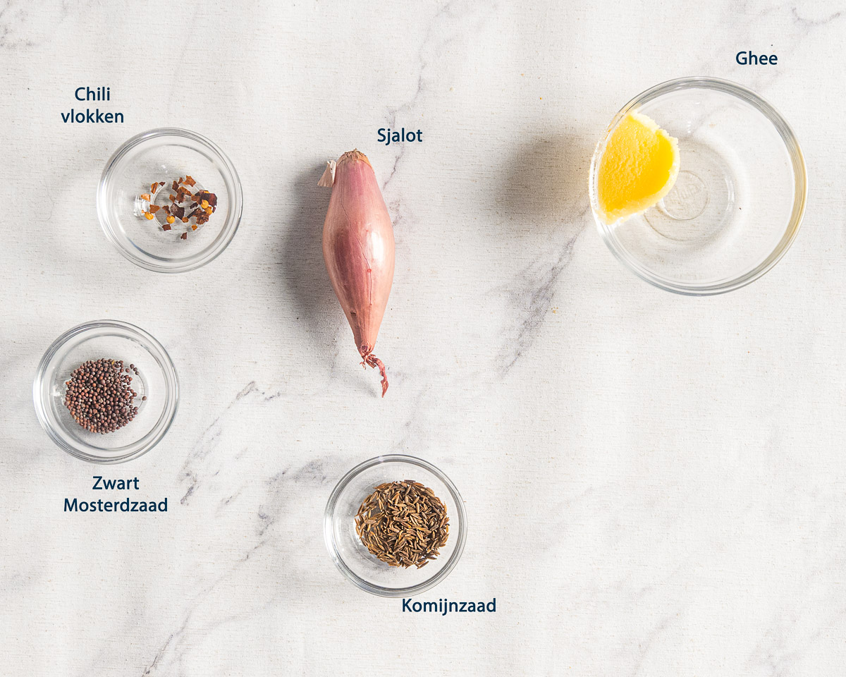 Ghee, sjalot, chilivlokken, zwart mosterdzaad en komijnzaad voor tadka, met Nederlandse labels.