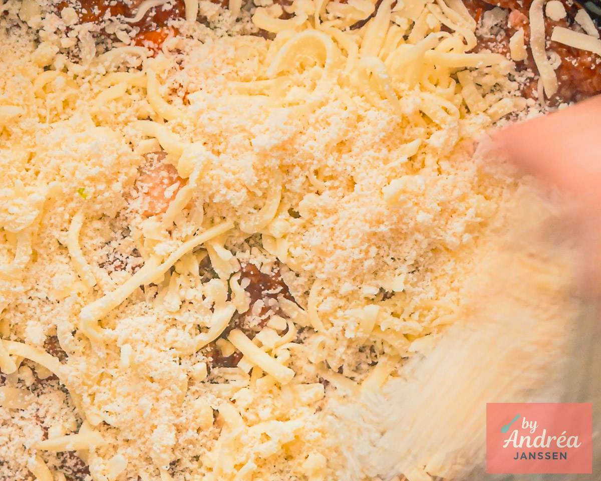 Geraspte mozzarella en Parmezaanse kaas worden over de lasagne in de slowcooker verdeeld.