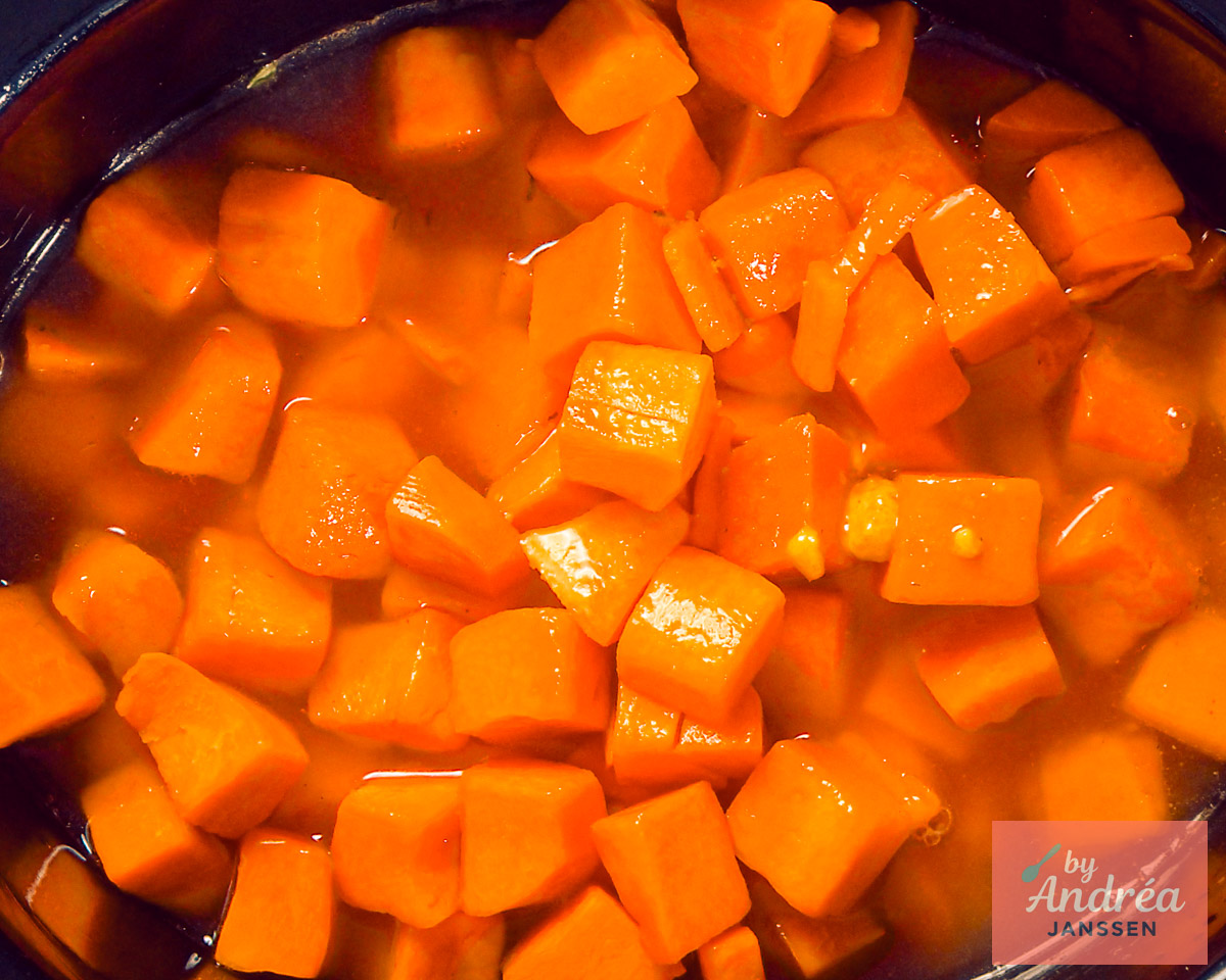 Pompoenblokjes in bouillon in de open slowcooker, gezien van bovenaf.