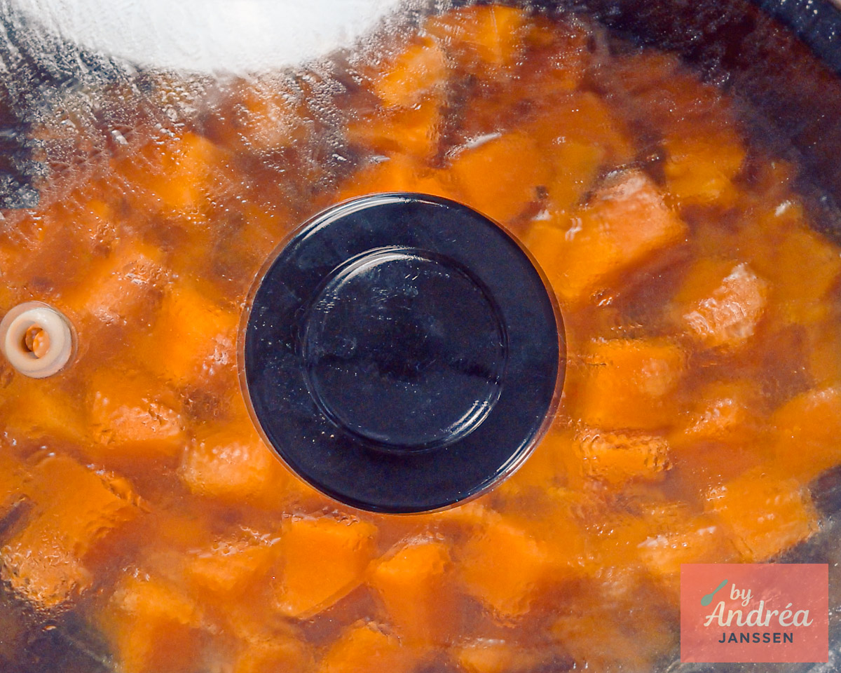 Pompoenblokjes in de slowcooker onder een glazen deksel met condensdruppels.