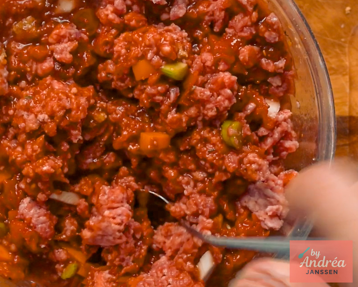 Rundergehakt wordt met tomatensaus, wortel en bleekselderij gemengd in een glazen kom.