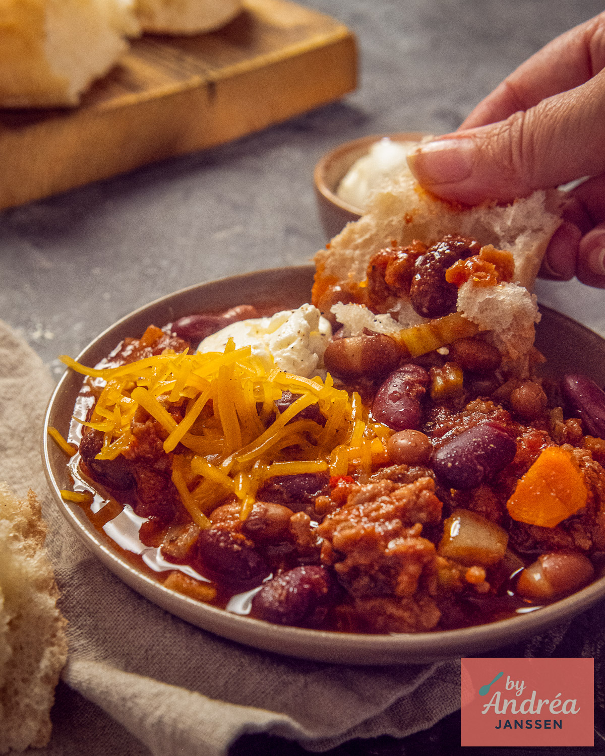 Kom slowcooker chili con carne met gehakt, bonen, cheddar en zure room, met een stuk brood om te dippen.