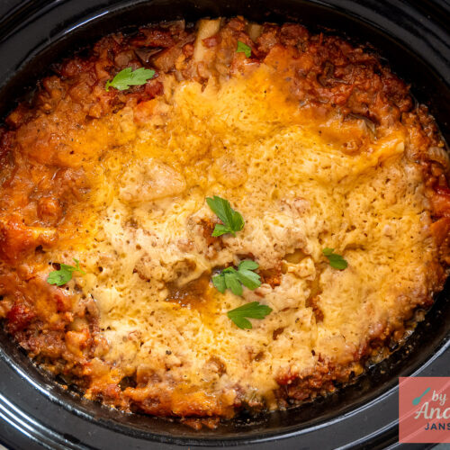 Lasagne met gesmolten kaas, tomatensaus langs de randen en peterselie, van bovenaf in de slowcooker.