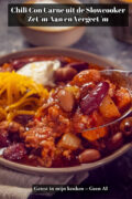 Chili con carne uit de slowcooker geserveerd in een kom met geraspte cheddar en zure room, opgeschept met een lepel