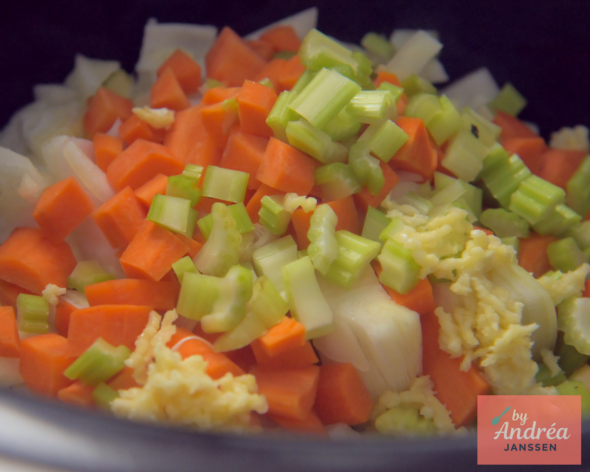 Stukjes wortel, bleekselderij, ui en knoflook in de pot voor chili con carne uit de slowcooker.