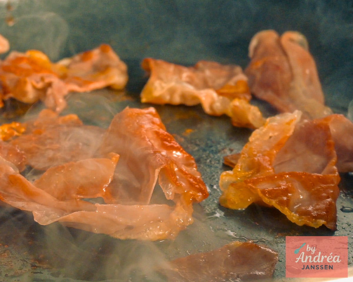 Dunne plakjes prosciutto bakken in een koekenpan, met goudbruine, omgekrulde randjes.