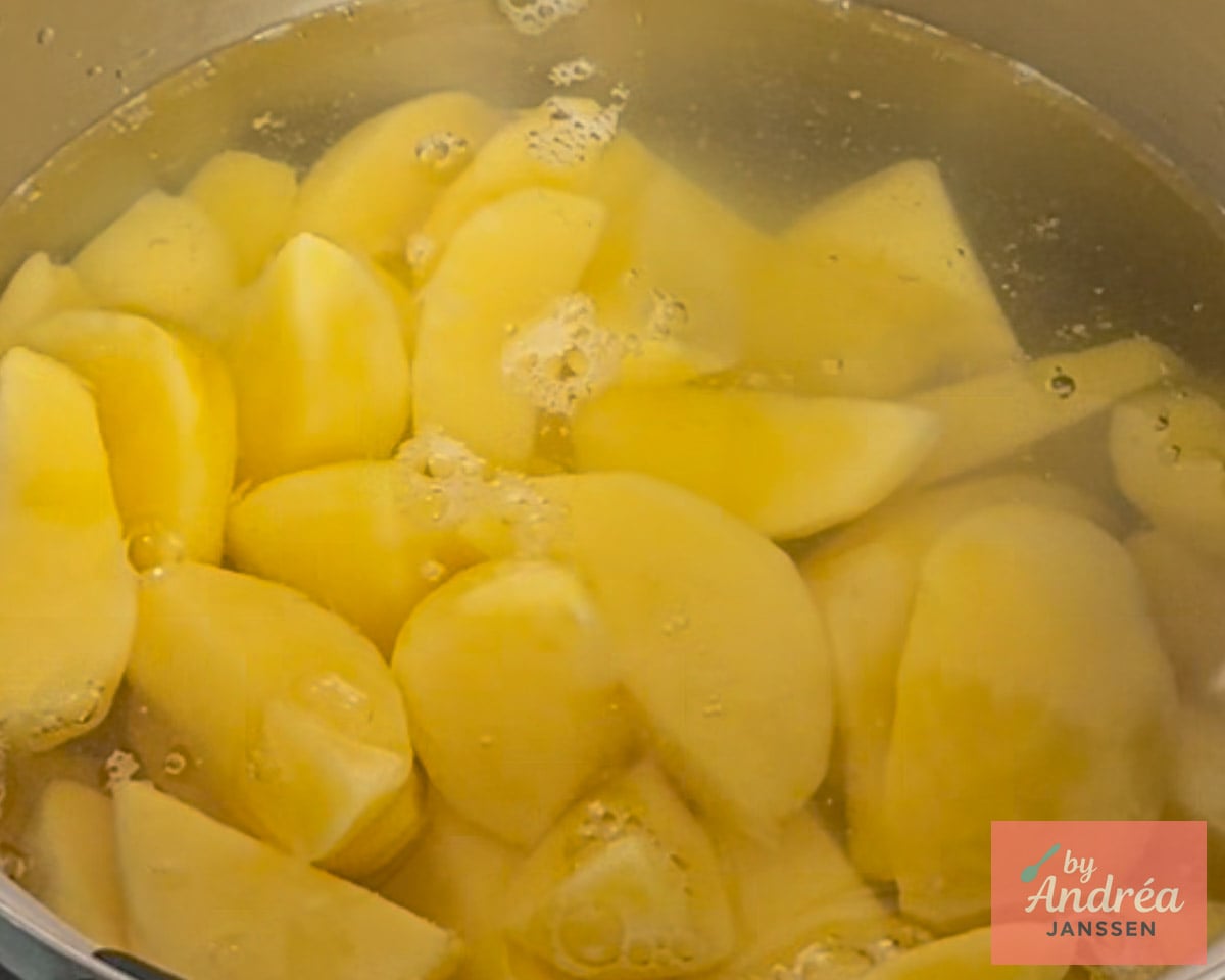 Geschilde aardappelen in stukken liggen in een pan met water en kleine belletjes aan het oppervlak.