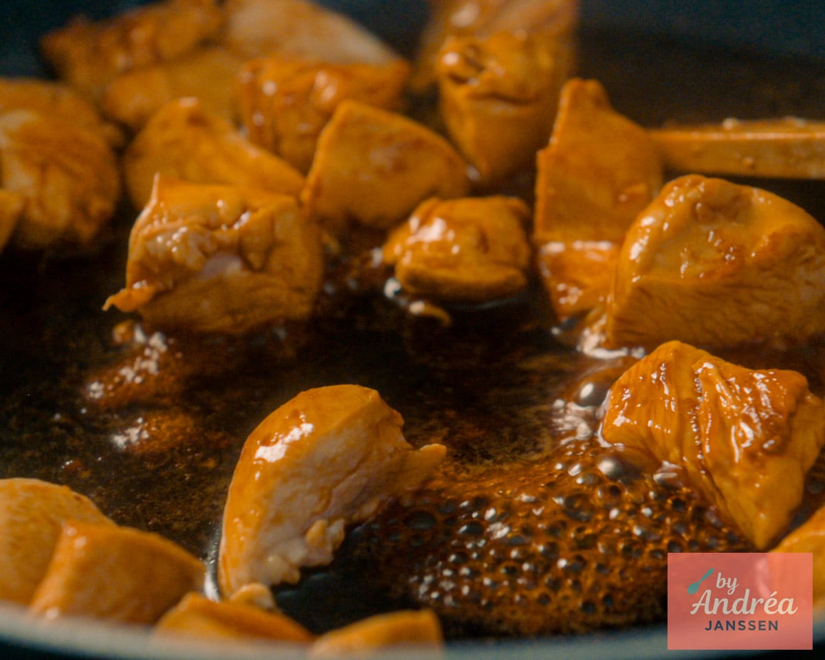 Stukjes kipfilet in glanzende, donkerbruine ketjapsaus die borrelt in een koekenpan.